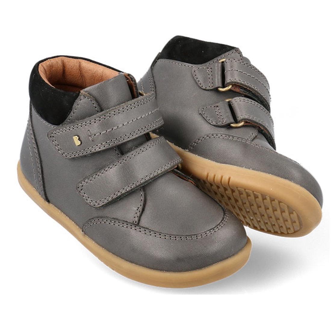 The Bobux Iwalk Timber Charcoal Grey Leather Boot 632624 is a unisex pair made from premium full grain leather, featuring tan rubber soles and two adjustable strap closures. One boot stands upright while the other tilts slightly forward.