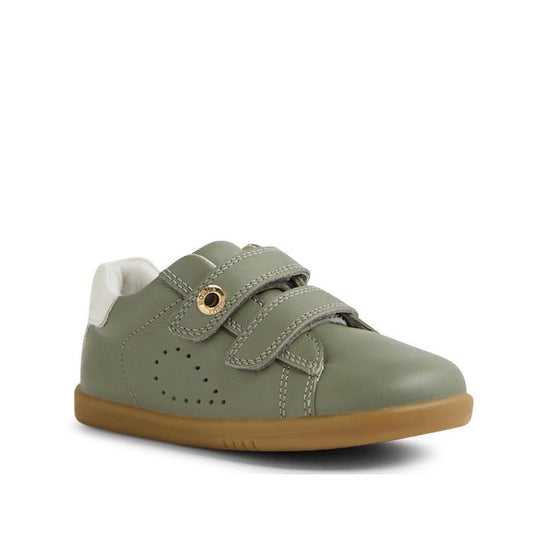 The Bobux IW Iwalk Maverick Leather Sneaker in Vetiver Green features a tan rubber sole, white heel accent, dual Velcro straps, decorative stitching, side perforations, and breathable leather for all-day comfort.