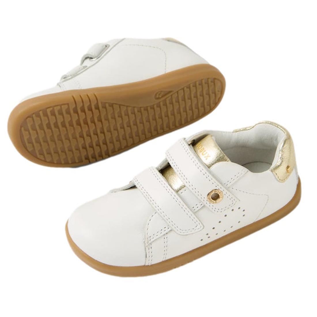 The Bobux IW Iwalk Maverick Leather Sneaker in White Gold features kids’ leather uppers, light brown rubber soles, gold accents on the heel and tongue, and two adjustable straps. One toddler sneaker stands upright; the other displays its sole., 9420074836