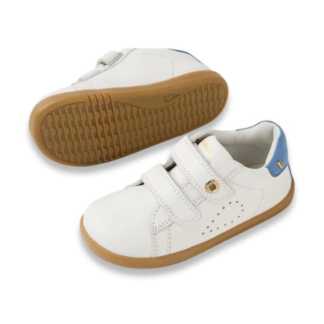 The Bobux IW Iwalk Maverick Leather Sneaker in White and Coronet Blue features white leather, tan rubber soles, blue heel accents, and two velcro straps. Displayed on a white background; one shoe is upright while the other shows the sole., 9420074836588, 