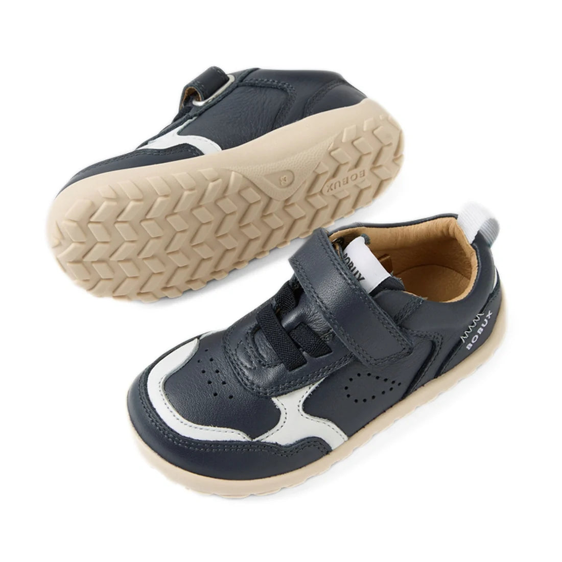 A pair of Bobux IW Iwalk Neo Toddlers Leather Sneaker Navy Barefoot are shown: both sneakers feature navy blue and white leather uppers with beige soles. One shoe is upright, highlighting its top and side, while the other is flipped to display the tread p
