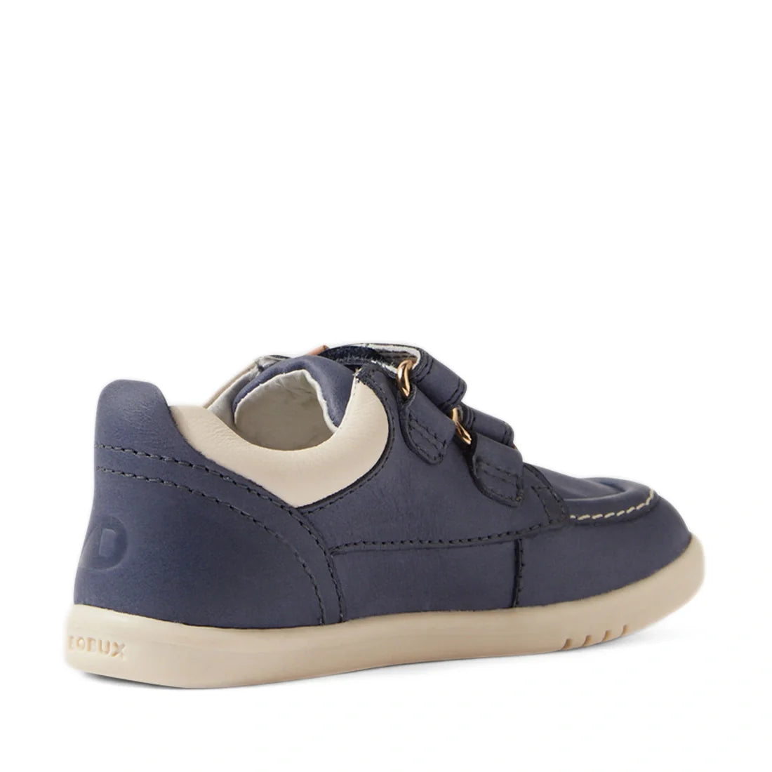The Bobux IW Iwalk Oakley Toddlers Leather Sneaker in Vintage Blue features a navy hue, beige lightweight sole, and padded collar, shown from a back side angle. Designed with two hook-and-loop straps, detailed stitching, and moccasin boat shoe-inspired ac