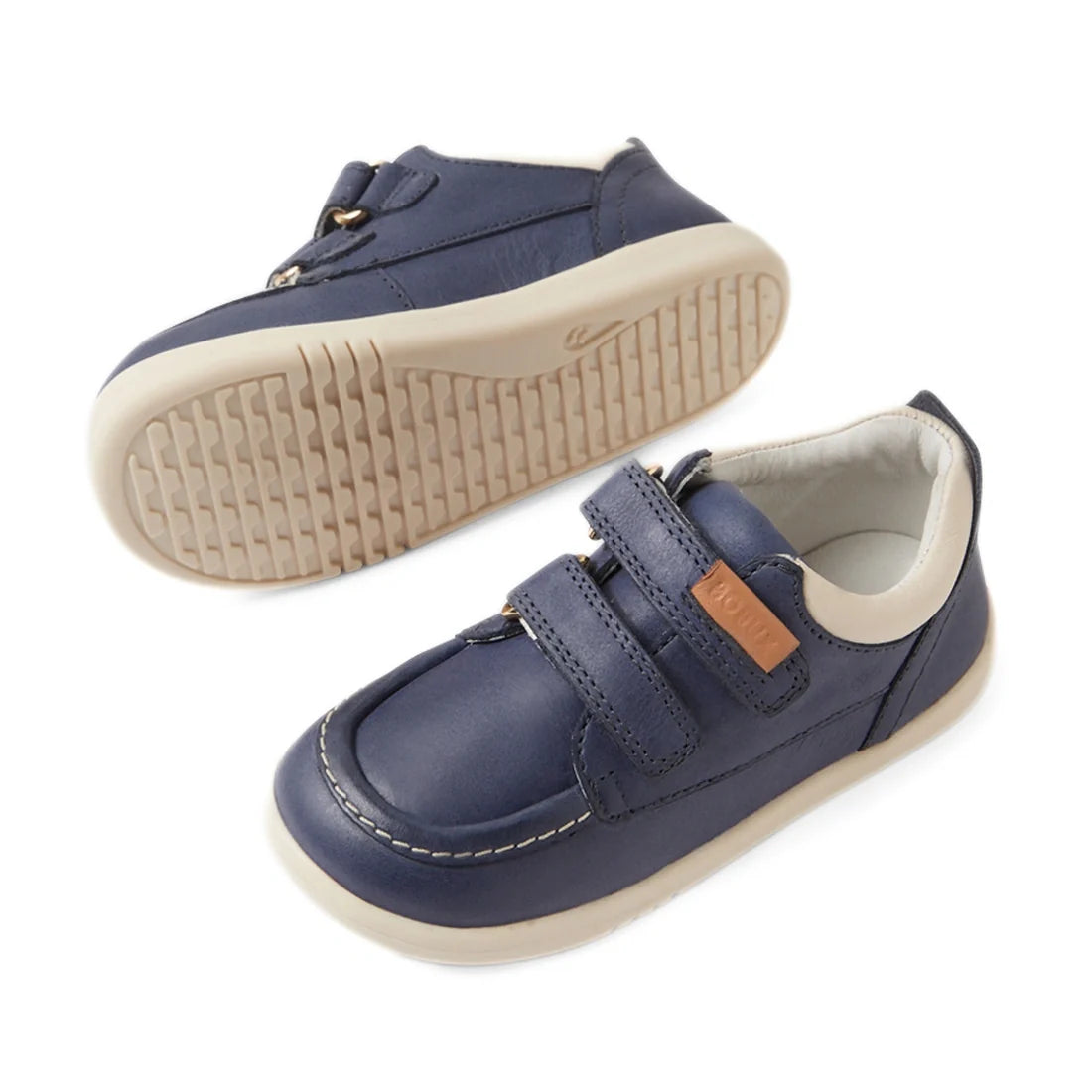 Two vintage blue Bobux IW Iwalk Oakley toddlers’ leather sneakers, featuring white soles and Velcro straps, with one shoe displayed from the side and the other showing the sole. These classic moccasin boat shoe-style sneakers include white stitching detai