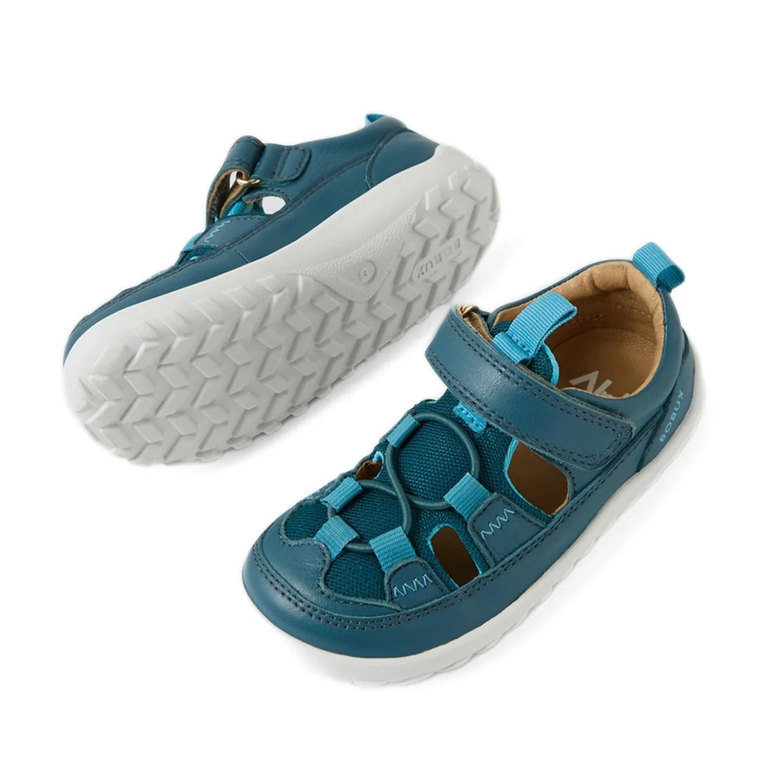 Bobux IW Iwalk Rocky Mediterranean Green Closed Toe Sandal Barefoot features a green leather design with white rubber soles, Velcro straps, closed toes, and cut-out sides. One sandal is upright and the other is flipped to reveal the sole’s textured patter