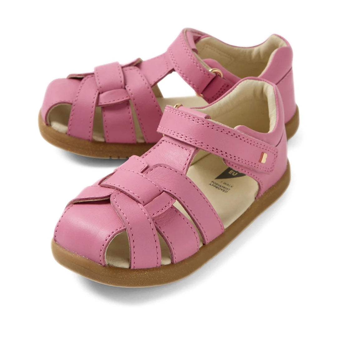 The Bobux IWalk Skip Twist Sandal in Cashmere Rose Pink is a closed-toe toddler sandal crafted from leather, featuring adjustable Velcro straps and sturdy brown rubber soles. Displayed on a white background, these stylish sandals offer comfort and durabil