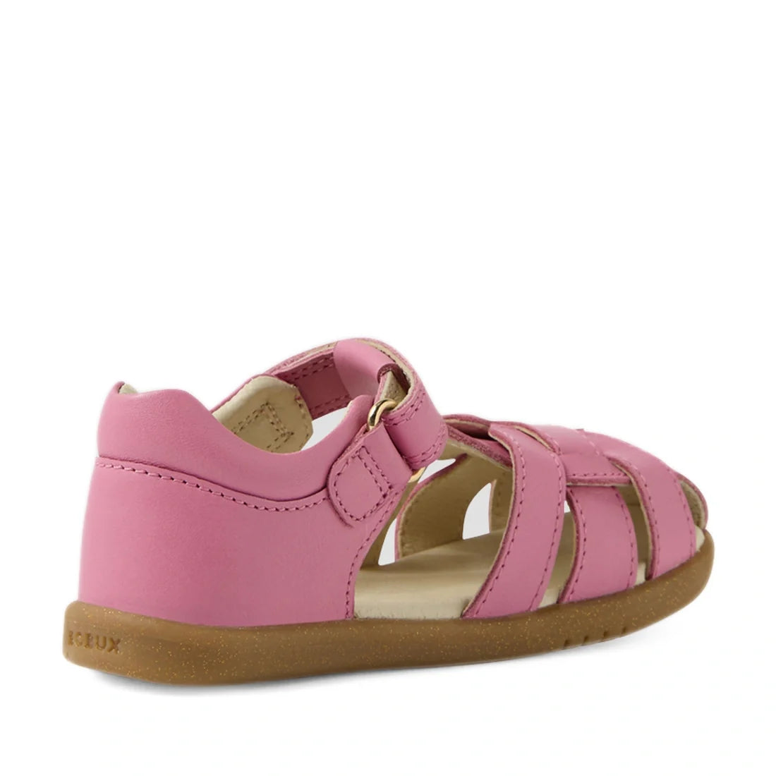 The Bobux IWalk Skip Twist Sandal in Cashmere Rose Pink for toddlers features a closed heel, open toe, and Velcro strap. Made from leather, it has a light brown sole with a textured bottom for improved grip and is shown from a back side angle., 9420074854