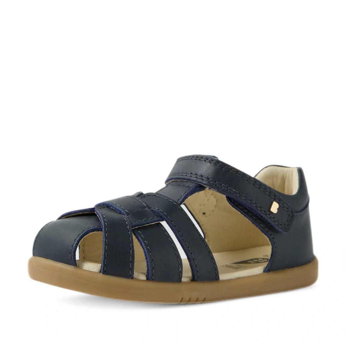 The Bobux IWalk Skip Twist Sandal in Navy features a closed toe design for toddlers, a tan rubber sole, and a secure velcro strap closure. These stylish and breathable kids’ shoes combine comfort and protection for little feet., 9420074854087, 94200748540