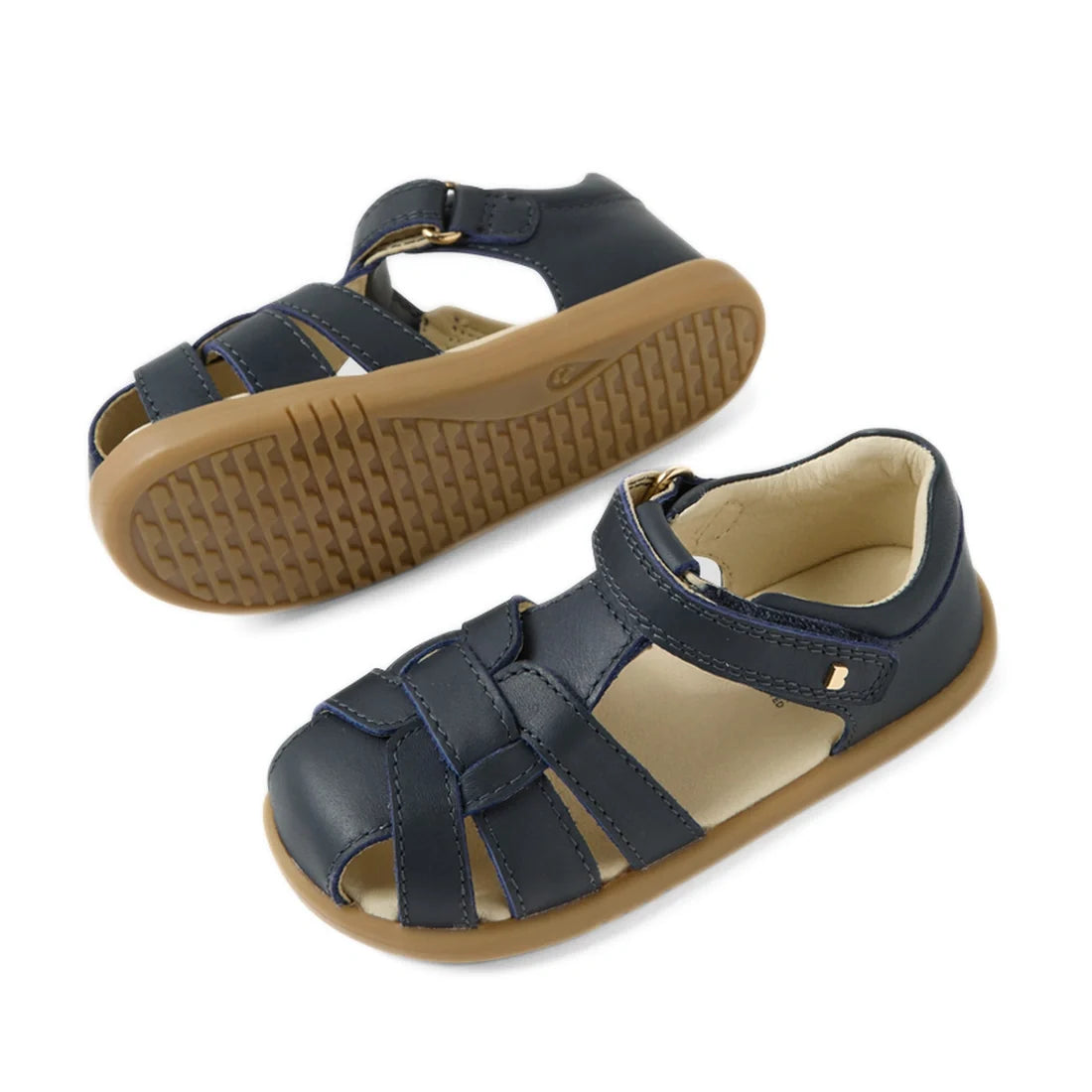 Bobux IWalk Skip Twist Sandal Navy Closed Toe Toddlers feature navy blue leather uppers, tan rubber soles, and a convenient hook-and-loop strap. Shown from both the side and bottom view, these breathable kids’ sandals provide comfort and protection for li