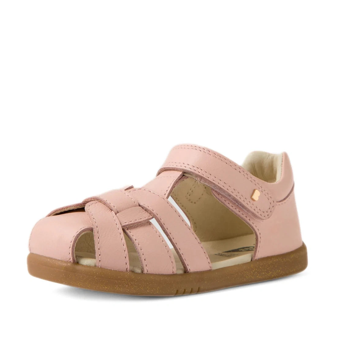 The Bobux IWalk Skip Twist Sandal in Cameo Rose Pink is a closed toe toddler leather sandal, designed with crisscross leather straps, side cutouts, a convenient velcro fastening, and a sturdy brown rubber sole—making it the ideal closed-toe sandal for act