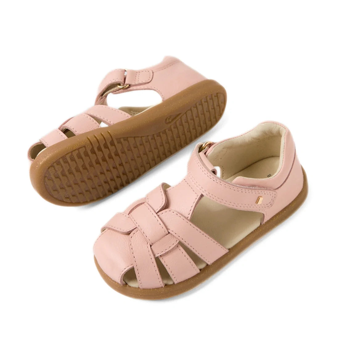 Introducing the Bobux IWalk Skip Twist Sandal in Cameo Rose Pink for toddlers, featuring closed toes, woven leather straps, easy velcro ankle closures, and durable brown rubber soles—viewed from both the side and bottom., 9420074854155, 9420074854162, 942