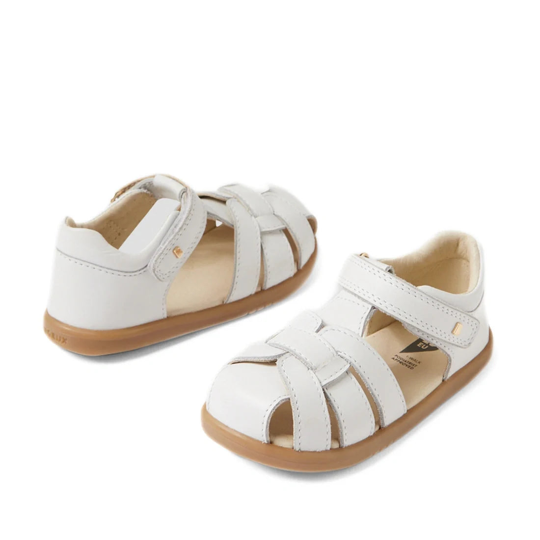 A pair of Bobux IWalk Skip Twist Sandal White Closed Toe Toddlers, featuring white leather uppers, tan rubber soles, Velcro straps, and a breathable design for kids, displayed on a plain white background.
