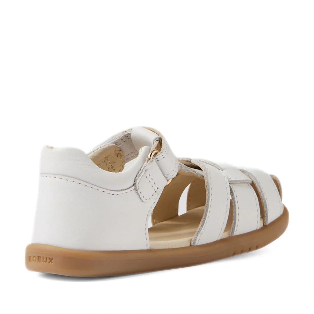A back left side view of the Bobux IWalk Skip Twist Sandal in white for toddlers showcases its leather construction, closed heel, open toe, adjustable velcro strap, and tan rubber sole. This breathable sandal offers a comfortable and stylish option for li
