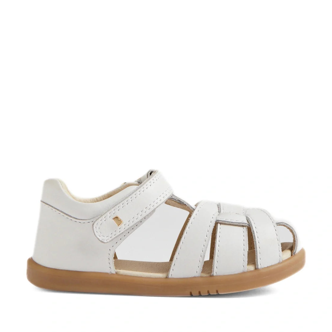 The Bobux IWalk Skip Twist Sandal in White for toddlers features a closed toe design, tan rubber sole, secure velcro strap, and stylish woven leather detailing across the front—these breathable kids’ sandals deliver both comfort and style for every advent