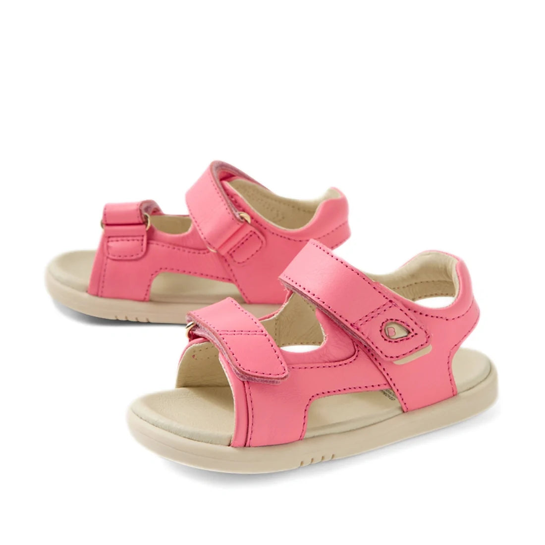 The Bobux IWalk Strand Sandal in Pink Lemonade is an open-toe leather sandal for toddlers, featuring adjustable velcro straps and beige soles. Shown at a slight angle on a white background, these stylish and comfortable sandals are perfect for little feet