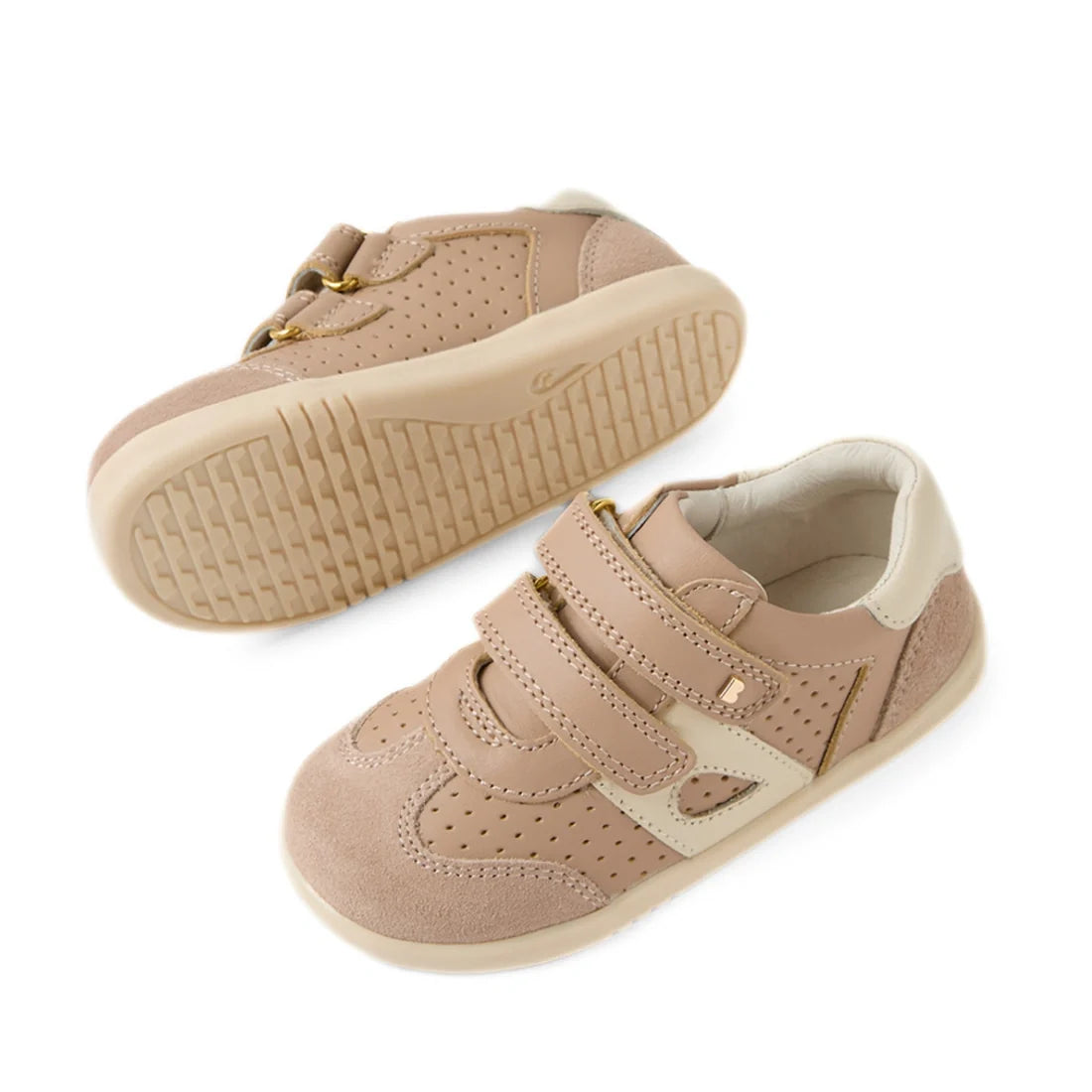 A pair of Bobux IW Iwalk Toddlers Titan Warm Taupe Leather Trainers are shown—one upright and one on its side displaying the slip-resistant rubber tread. These beige and cream leather sneakers feature adjustable hook-and-loop straps and perforated detaili