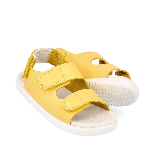 The Bobux Iwalk IW Quick Dry Topia Sandal 651304 Pineapple is a children's yellow leather sandal with white soles and two adjustable Velcro straps. One sandal stands upright, while the other tilts to reveal its textured white sole.