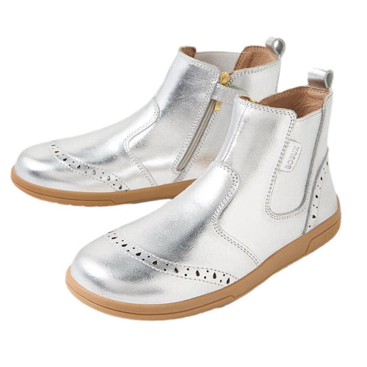 The Bobux Kid+ KP Billie 2 II Girls Leather Boot in silver features shiny leather, tan rubber soles, brogue detailing on the toe, side zippers, back pull tabs, and a flexible sole for all-day comfort.