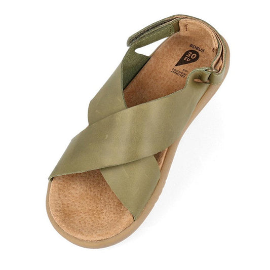 The Bobux Kid+ Plus Glide Sea Kelp Green Open Toe Sandal 851103 is an olive green kids' leather sandal with wide crisscross straps, a tan textured footbed, beige sole, closed heel, and adjustable hook-and-loop fastening strap.