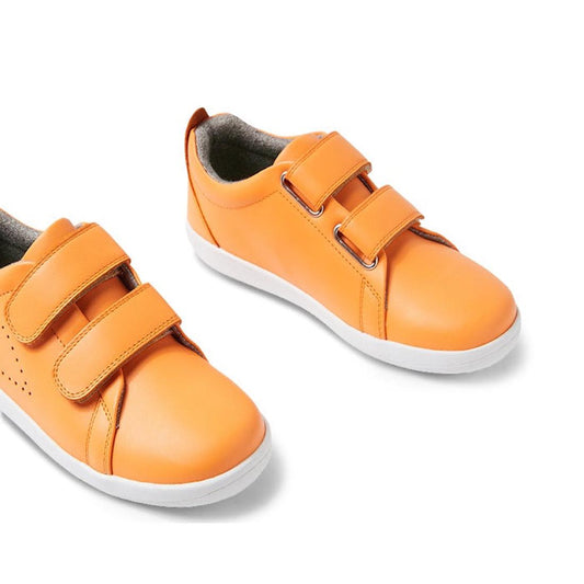 The Bobux KP Kid Plus Grass Court Apricot Crush 841009 are bright orange kids’ trainers with a durable leather upper, white soles, and two adjustable double Velcro straps, shown on a white background.