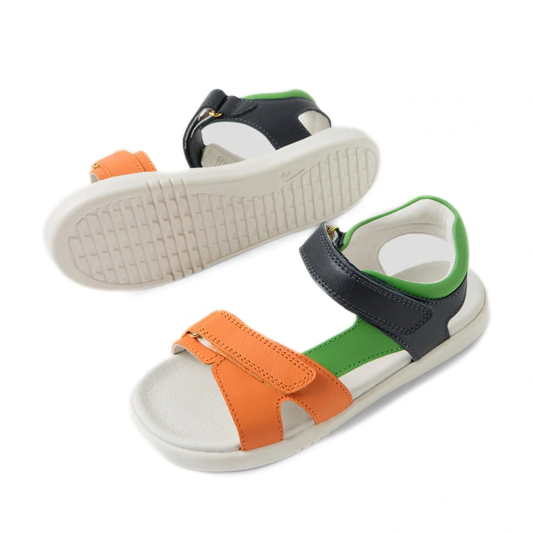 A pair of Bobux KP Kids Plus Dune Leather Sandal Navy for children features navy blue adjustable straps, green lining, and white soles. These breathable summer sandals are crafted for comfort and style—one sandal stands upright while the other lies on its