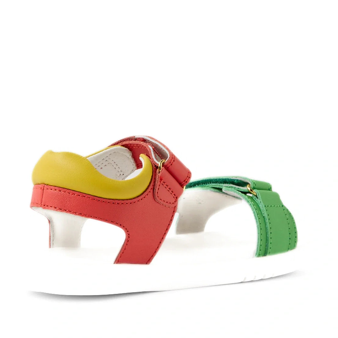 The Bobux KP Kids Plus Dune Leather Sandal Grenadine Red is a colorful kids’ leather sandal with a white sole, featuring red, green, and yellow leather straps with adjustable closures for a secure fit. The sandals are shown from the side and slightly behi