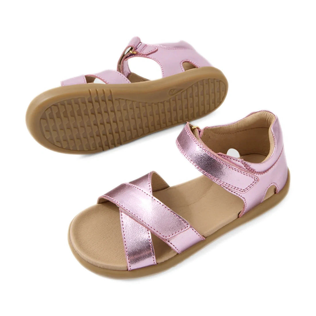 Two metallic pink Bobux KP Kids Plus Flora Leather Sandal Pink Lemonade kids sandals with tan soles are shown. One sandal is positioned upright, while the other displays the textured bottom. These adjustable leather sandals feature open toes and velcro st