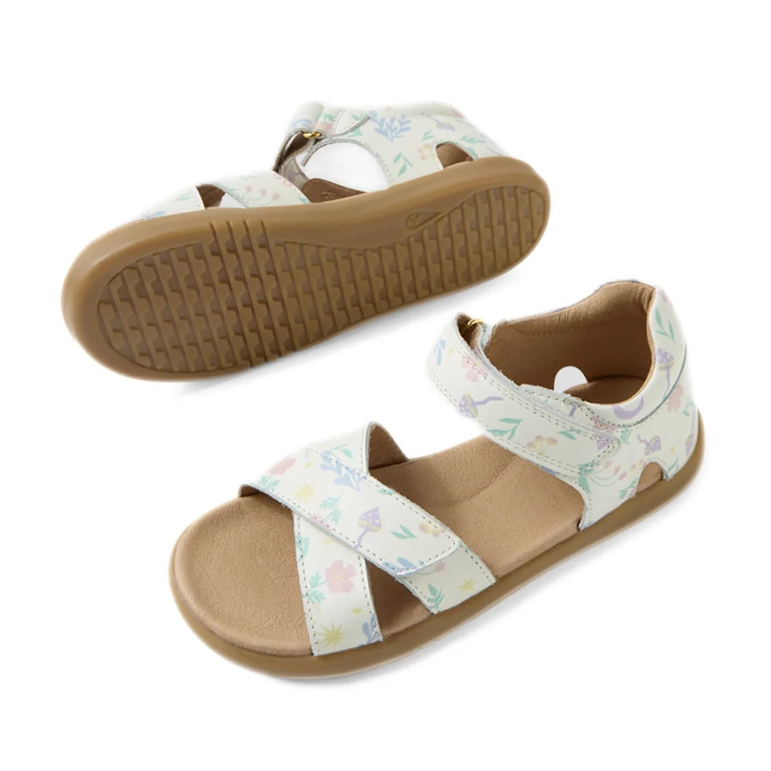 The Bobux KP Kids Plus Flora Leather Sandal in White Floral is an adjustable kids sandal featuring tan soles and white straps adorned with a pastel nature print of leaves and flowers. One sandal is displayed from the side, while the other is shown from th