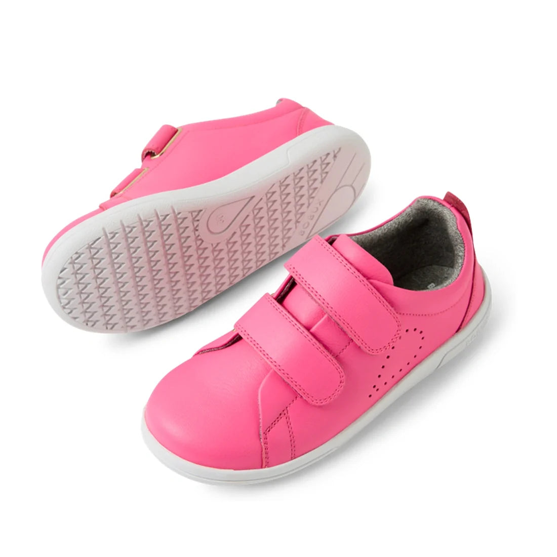 A pair of Bobux KP Kids Plus Grass Court 2 II Leather Sneakers in Pink Lemonade—crafted from leather with white soles and two velcro straps. One sneaker stands upright while the other rests on its side, showcasing the textured sole pattern—a vibrant choic
