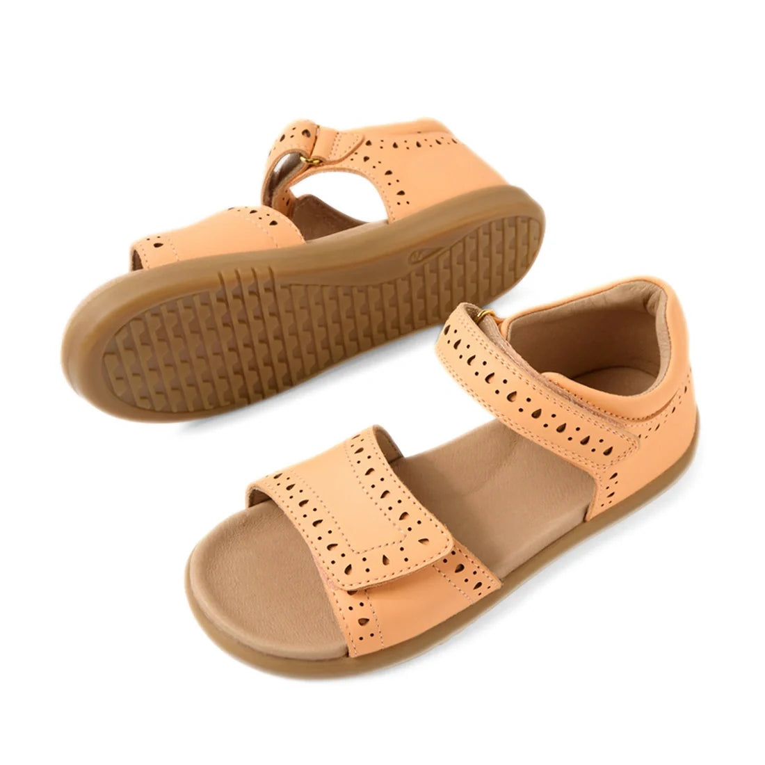 A pair of Bobux Kid+ Plus KP Logan Peach Jelly Open Toe Sandals featuring light brown leather, perforated detailing, adjustable hook-and-loop straps, and rubber soles. One kids’ sandal stands upright while the other lies on its side, displaying the sole’s