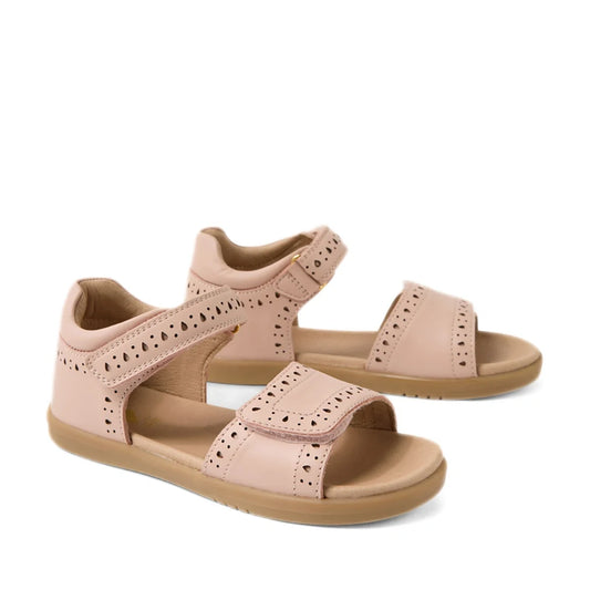 A pair of Bobux Kid+ Plus KP Logan Cameo Rose Pink Open Toe Sandals for girls, featuring light brown soles, stylish cut-out patterns, and adjustable Velcro straps over the toes and around the ankles. These leather sandals provide both comfort and style fo