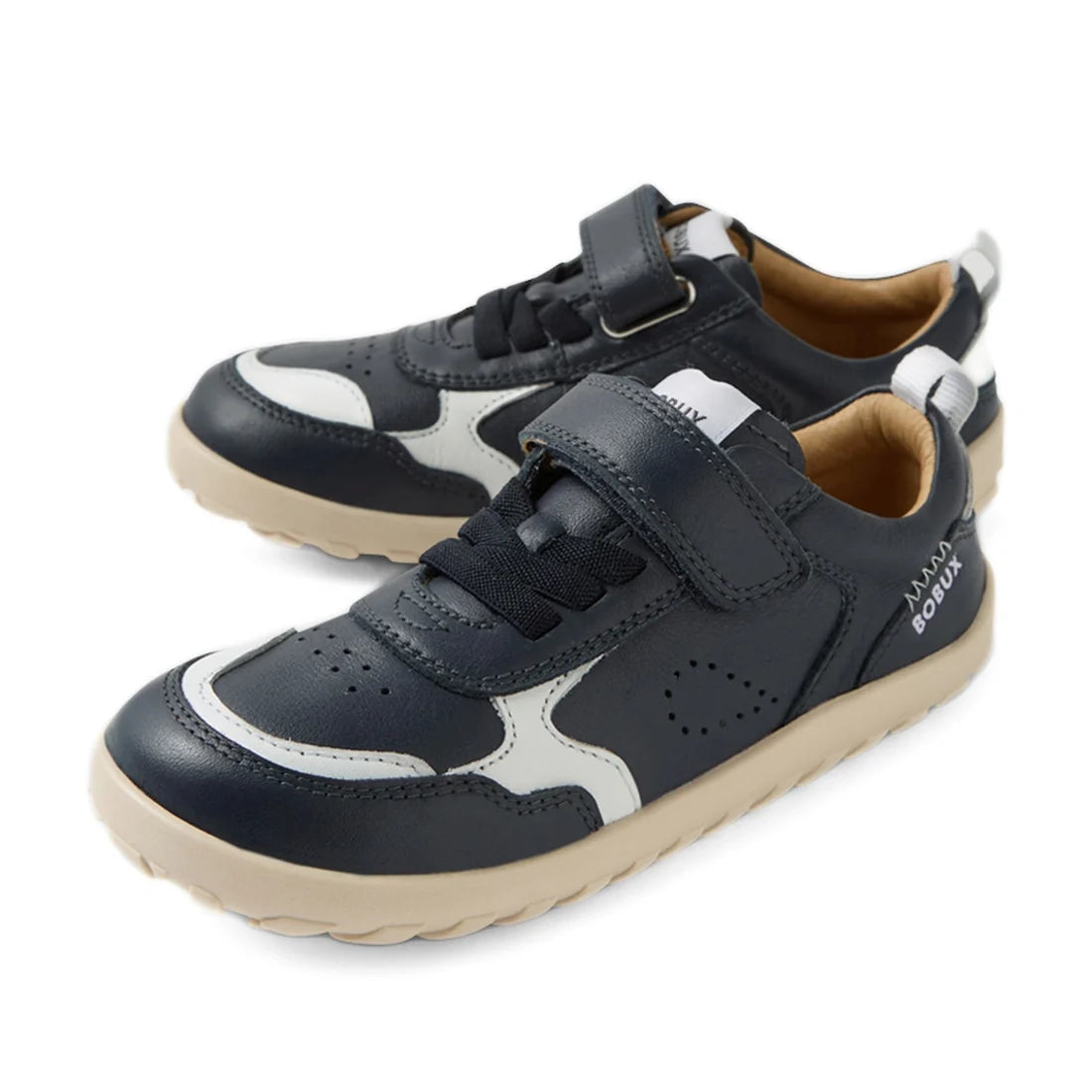 A pair of Bobux Kid+ Plus KP Neo Leather Sneaker Navy Alpha kids’ leather sneakers in navy blue and white, featuring beige soles, both laces and a velcro strap, a barefoot-shaped toebox, and a zero drop sole, displayed on a white background.