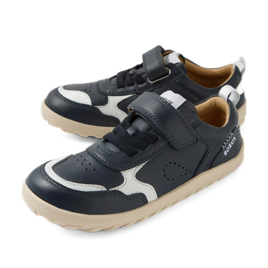 A pair of Bobux Kid+ Plus KP Neo Leather Sneaker Navy Alpha kids’ leather sneakers in navy blue and white, featuring beige soles, both laces and a velcro strap, a barefoot-shaped toebox, and a zero drop sole, displayed on a white background.