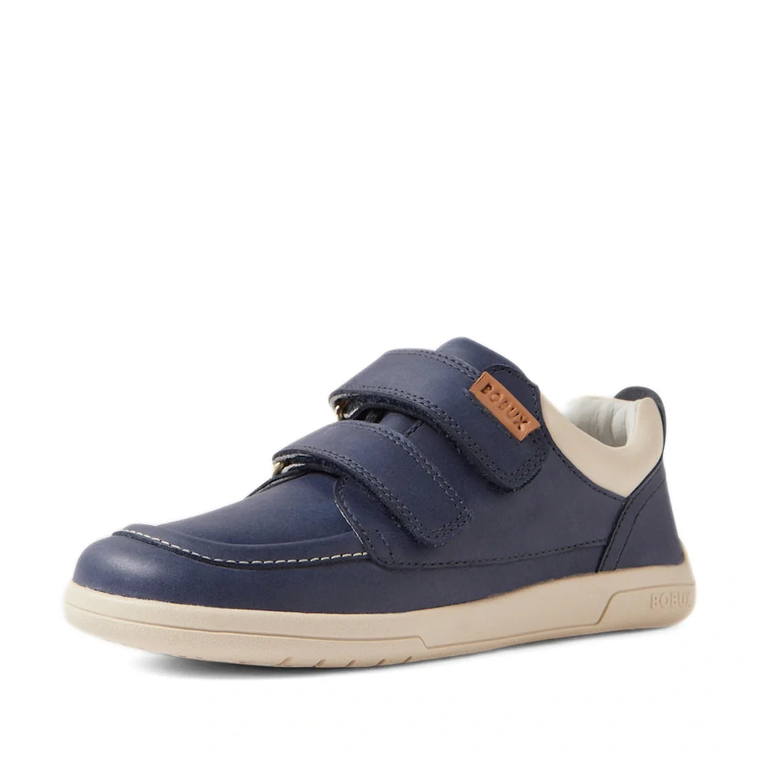 A stylish kids’ leather sneaker, the Bobux Kid+ Plus KP Oakley Leather Sneaker in Vintage Indigo Blue features a navy blue design with two Velcro twin-straps, a beige sole, and a small brown BOBUX label on the side. The shoe is photographed at an angle to