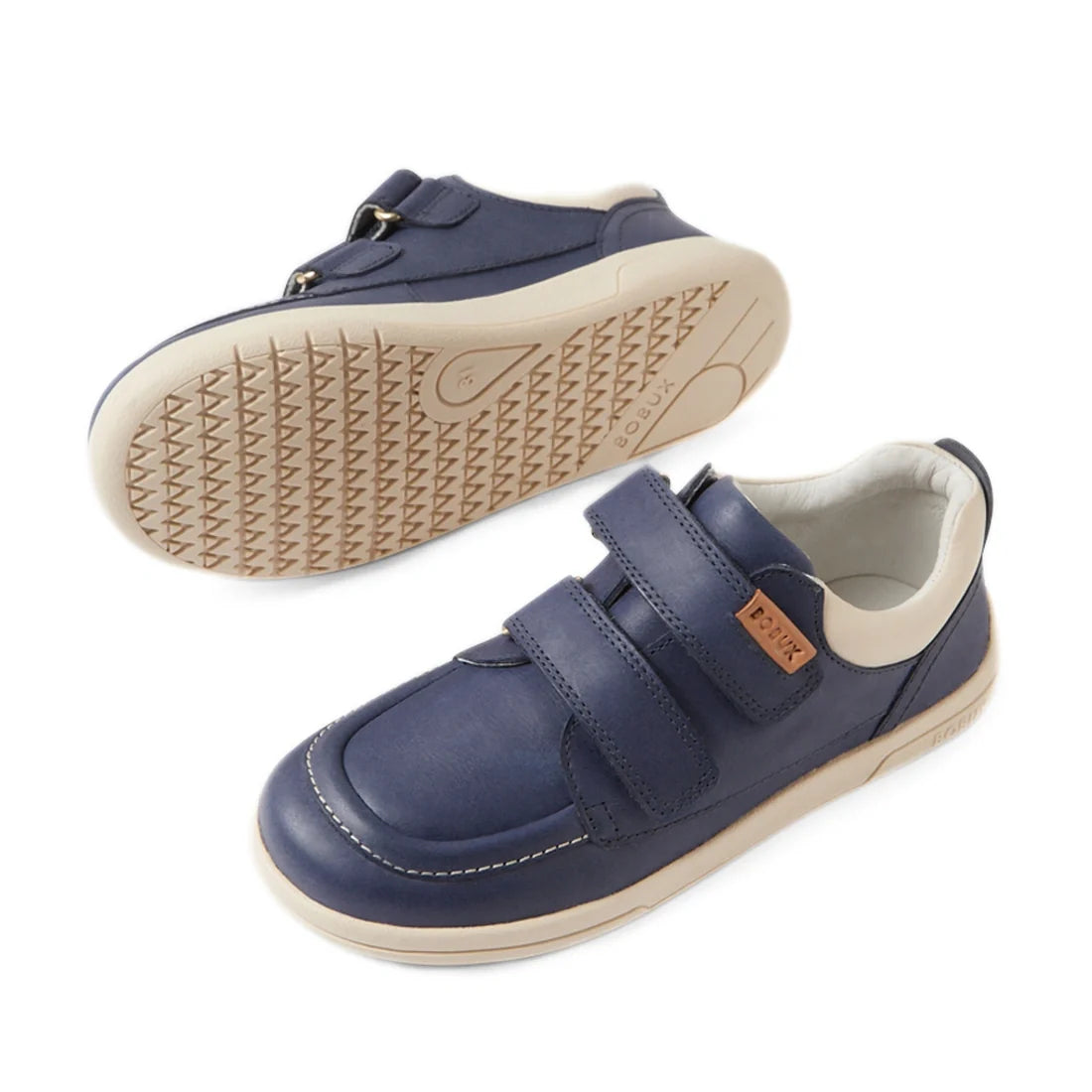 Bobux Kid+ Plus KP Oakley Leather Sneaker in Vintage Indigo Blue—children’s sneakers inspired by classic boat shoe design, featuring beige soles, twin-strap Velcro closures, and a small brown tag on the side; shown from a side and bottom view., 9420074848