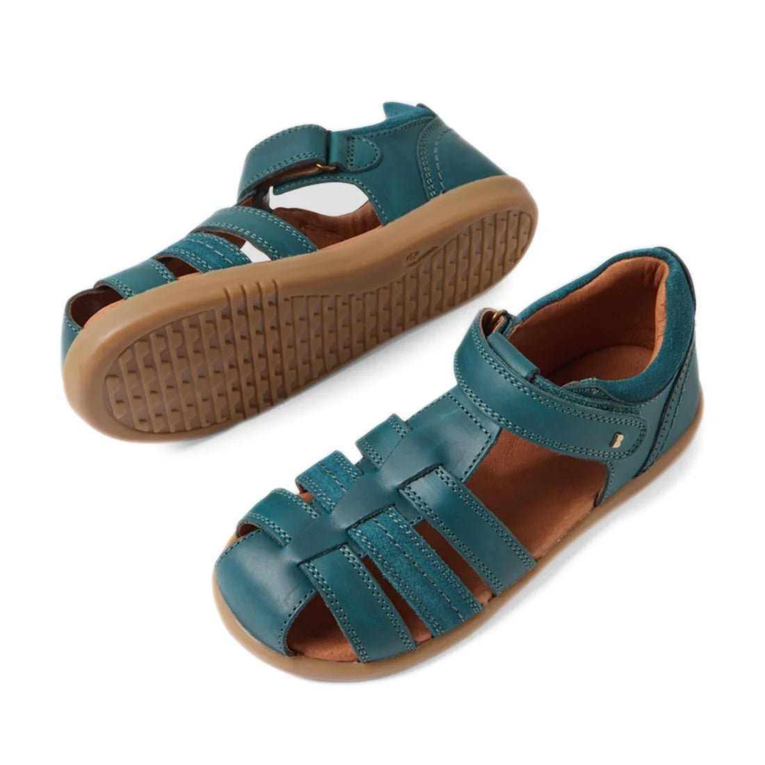 A pair of Bobux Kid+ Plus Roam Mediterranean Green Closed Toe Sandals for kids, featuring tan rubber soles and adjustable Velcro straps. One sandal is upright while the other displays the textured sole—perfect leather summer sandals for active little feet