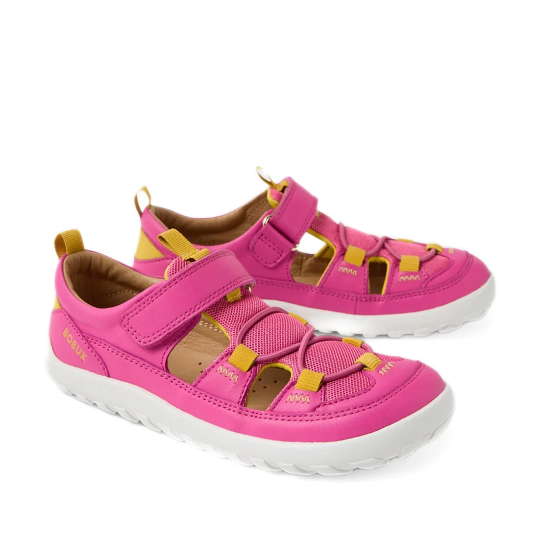The Bobux Kid+ KP Rocky Leather Closed Toe Sandal in Rose Violet is a pair of kids’ leather sandals featuring a bright pink and yellow (Rose Violet) colorway, barefoot-like zero drop design, white soles, velcro straps, and yellow pull tabs at the heel and
