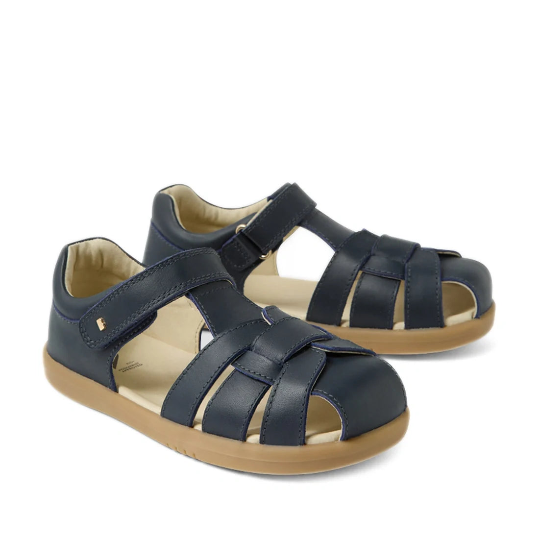 Introducing the Bobux Kids Plus KP Skip Twist Navy Closed Toe Sandal—featuring a navy blue design, tan rubber sole, and adjustable Velcro straps. These sandals are perfect as breathable summer footwear for active children.