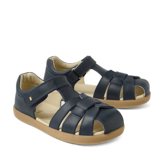 Introducing the Bobux Kids Plus KP Skip Twist Navy Closed Toe Sandal—featuring a navy blue design, tan rubber sole, and adjustable Velcro straps. These sandals are perfect as breathable summer footwear for active children.