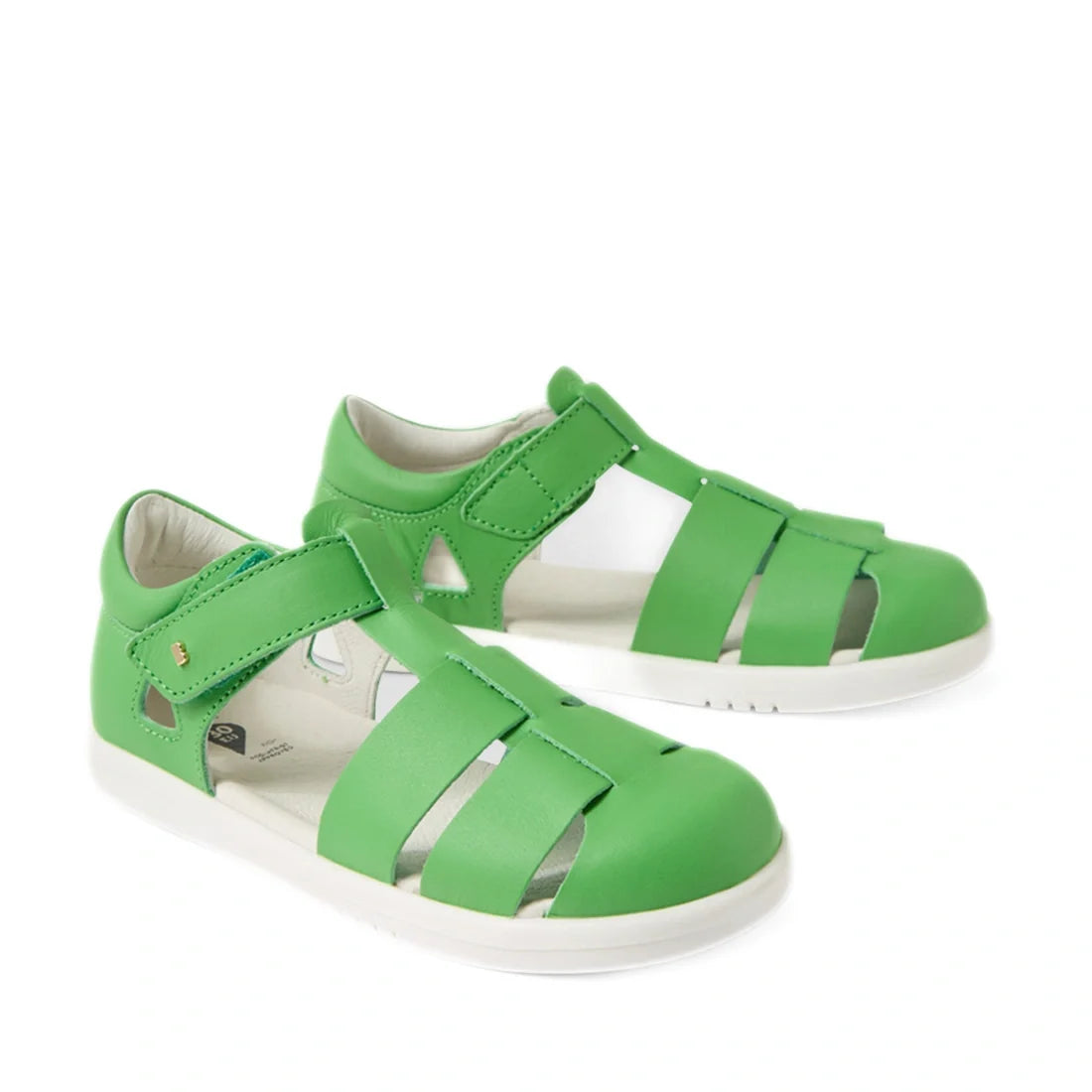 A pair of Bobux Kid + Plus Tidal Closed Toe Quick Dry Sandal Retro Green for kids, featuring green uppers, white soles, and velcro straps, are stylishly displayed on a white background.