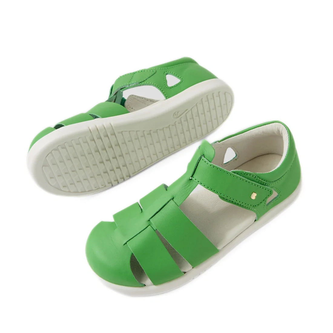 A pair of Bobux Kid + Plus Tidal Closed Toe Quick Dry Sandals in Retro Green, featuring white soles—one displayed from the side and the other showing the tread pattern from below. These stylish leather sandals are perfect for active kids, offering comfort