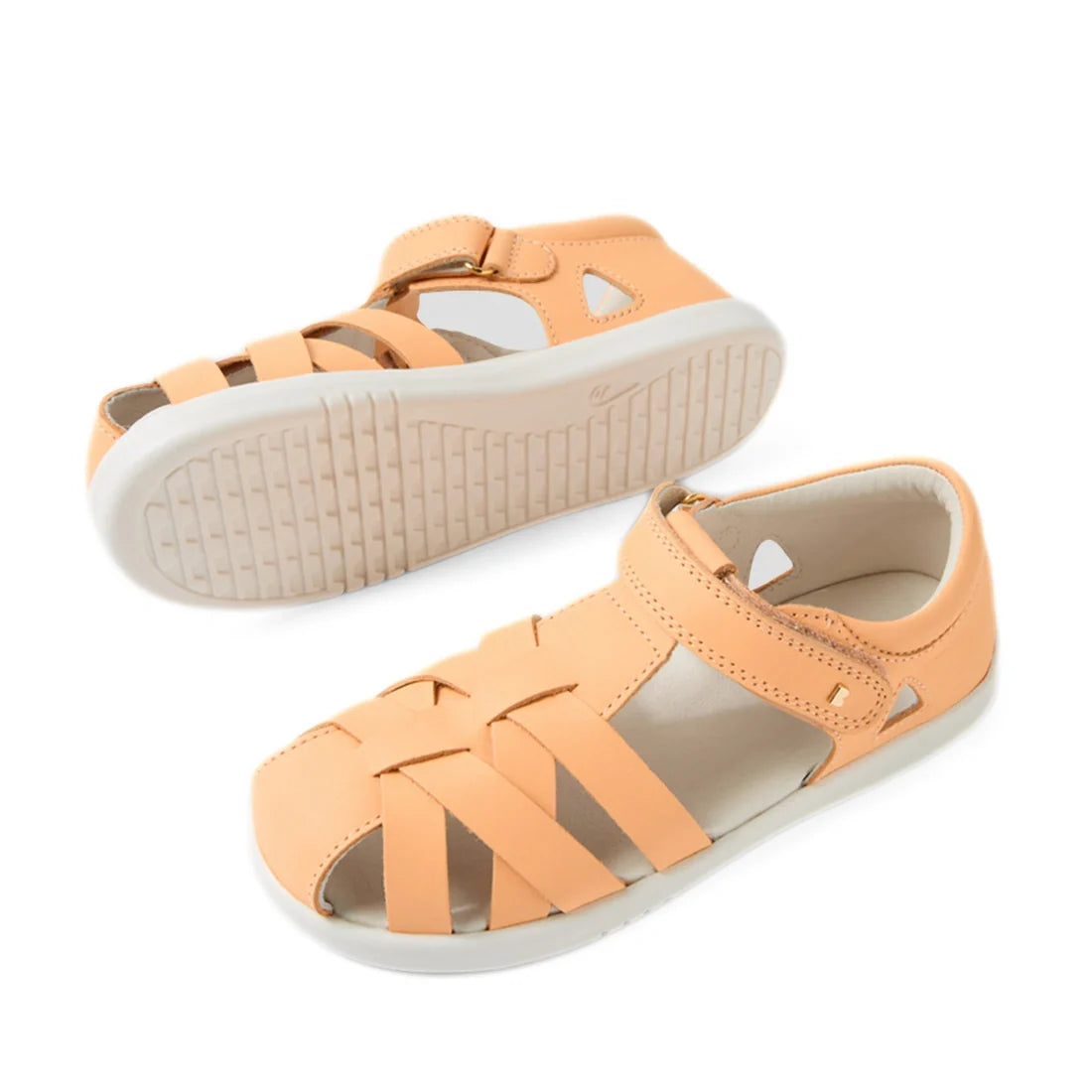 A pair of Bobux Kids Plus KP Tropicana II Peach Jelly Quick Dry Sandals, featuring a peach hue, closed-toe leather design with crisscross straps, white soles, and a hook-and-loop ankle strap. One sandal is pictured in profile while the other displays the 