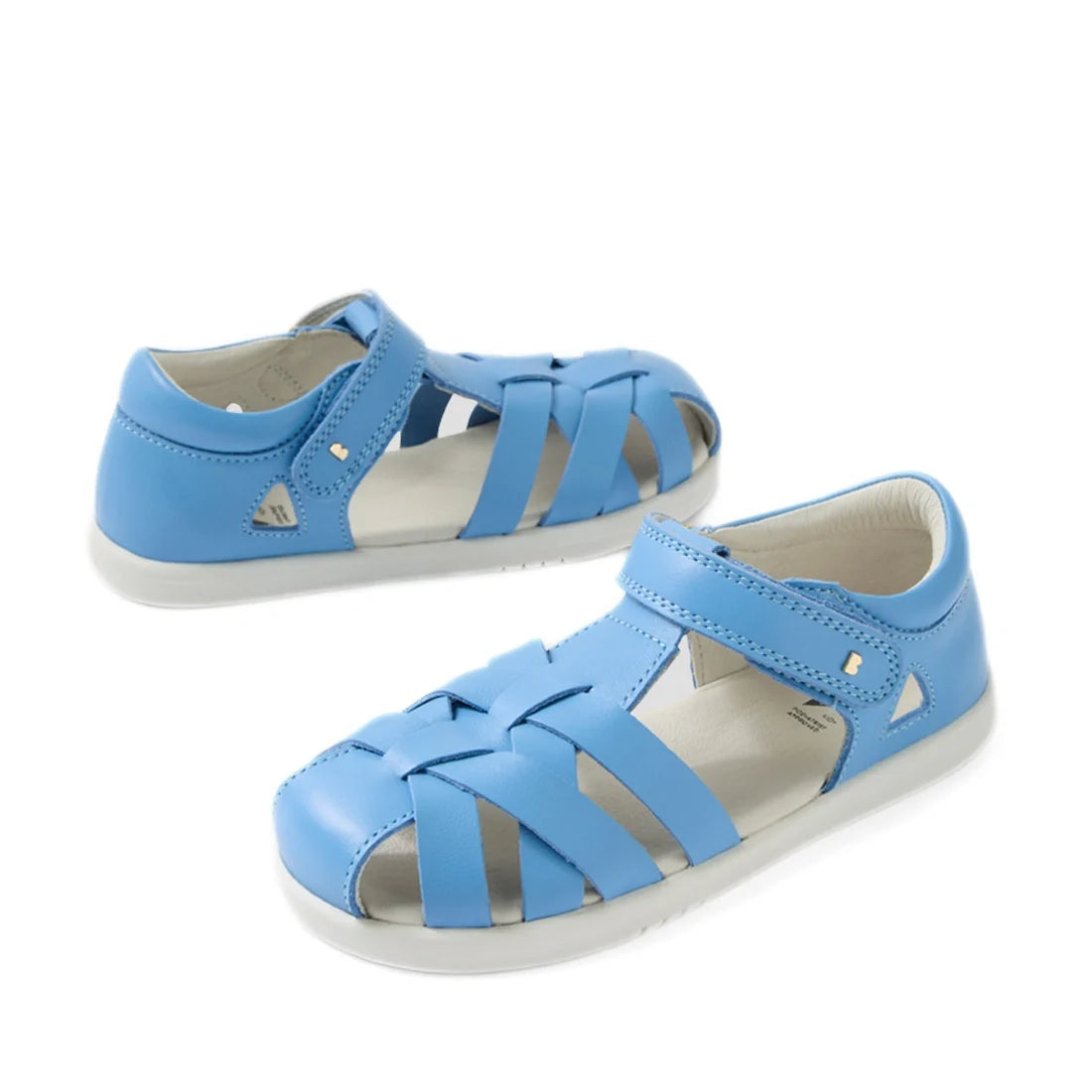 The Bobux Kids Plus KP Tropicana II Baltic Sea Blue Quick Dry Sandal is a pair of stylish children’s summer shoes featuring light blue closed-toe woven leather straps, white soles, and convenient Velcro closures, displayed on a white background.