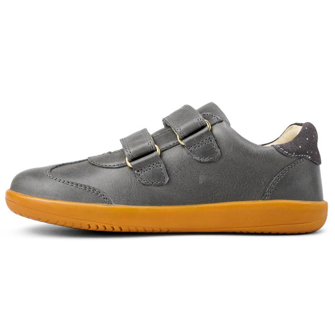 The Bobux Kids Plus KP Sprite Sneaker Charcoal Grey, from the winter 2023 collection, features two Velcro straps and a yellow-orange textured sole. Shown in left profile against a white background, these unisex shoes combine style, comfort, and durability
