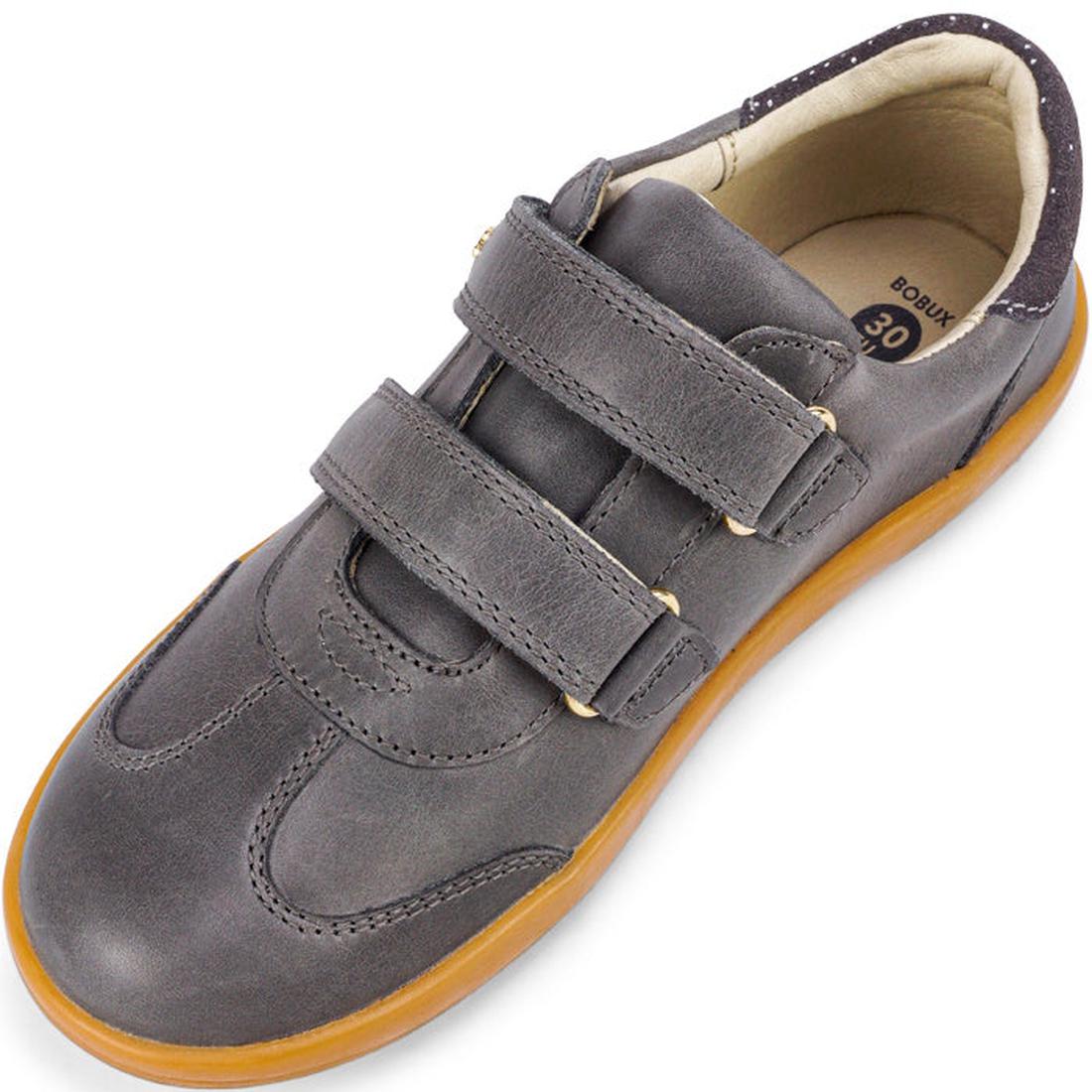 The Bobux Kids Plus KP Sprite Sneaker Charcoal Grey features two Velcro straps, a tan rubber sole, and a light inner lining—seen from above at an angle—making it an ideal unisex choice for winter 2023., 9420071316724, 9420071316731, 9420071316748, 9420071