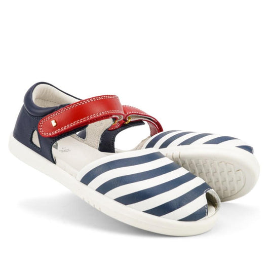 The Bobux Kid + KP Twist Open Toe Sandal Navy features navy and white stripes, a closed back for heel support, white soles, a red strap with gold buckle, and premium leather with an open toe for breathability.