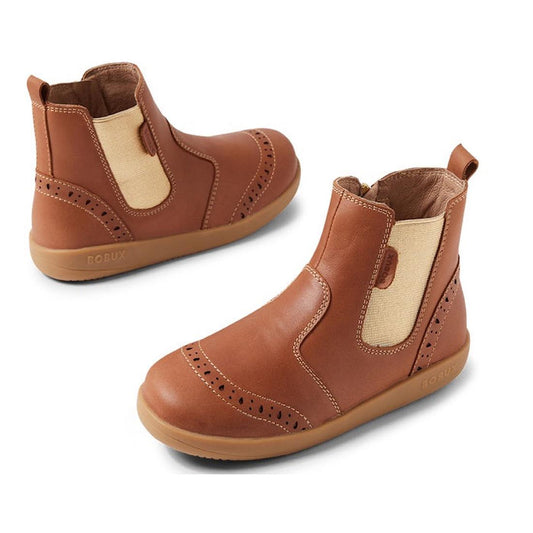 The Bobux Kid+ KP Billie II Girls Leather Boot in Caramel Tan is shown from various angles, featuring beige elastic side panels, brogue detailing on the toe and sides, a flexible sole, and tan rubber soles on a white background.