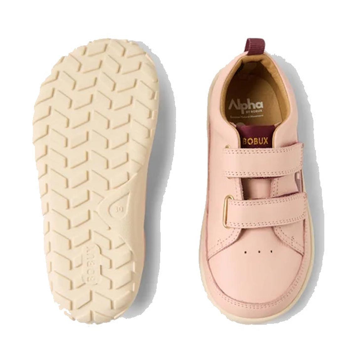 The Bobux Kid+ Dawn Leather Sneaker Cameo Rose Pink Alpha is shown with one shoe displaying the barefoot-shaped toe-box and branding, and the other flipped to highlight its textured cream-colored sole. Both feature two Velcro straps., 9420068565647, 94200
