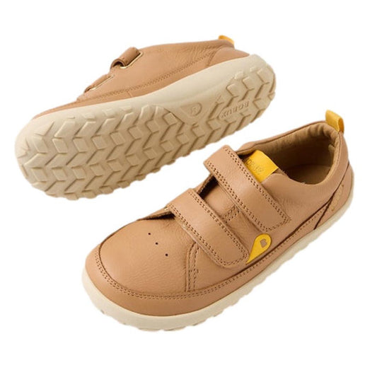 The Bobux Kid+ Dawn Leather Sneaker Sandstorm 854303 is a light brown children's sneaker with white rubber soles, yellow pull tabs, a barefoot-shaped toe-box, and two hook-and-loop Velcro straps, shown on a white background.