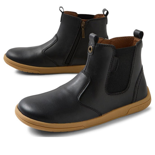The Bobux KP Kids Plus Jodhpur II Juniors Leather Boot in black features tan rubber soles, side zippers, elastic panels, and heel pull tabs, displayed on a white background.