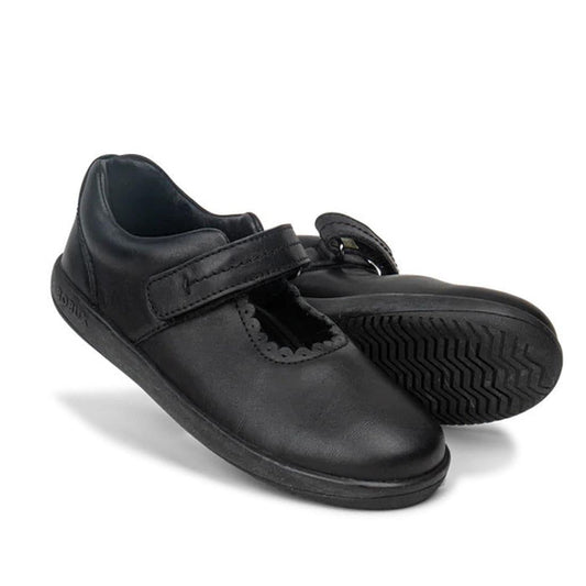 The Bobux Kid+ Black School Leather Shoe Journey Mary Jane is a durable kids’ school shoe in black leather with a Velcro strap, rounded toe, and scalloped edge. One stands upright while the other lays on its side to show the textured sole.